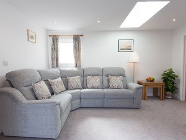 A living room with a gray sectional sofa with patterned pillows a floor lamp wooden nesting tables with a fruit bowl and a potted plant at Cornish Views in Camborne