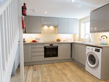 A kitchen with grey cabinets an oven a washing machine and wooden floors at Cornish Views in Camborne