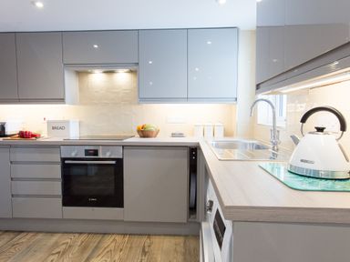 A kitchen with grey cabinets a built-in oven a stovetop a bread box a fruit bowl a kettle on the counter and a double sink at Cornish Views in Camborne
