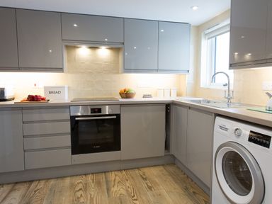 A kitchen with grey cabinets a built in oven a washing machine and a sink at Cornish Views in Camborne