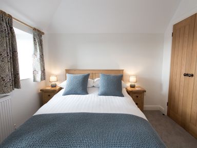 A bedroom with a double bed blue pillows and throw beside wooden nightstands with lamps at Cornish Views in Camborne