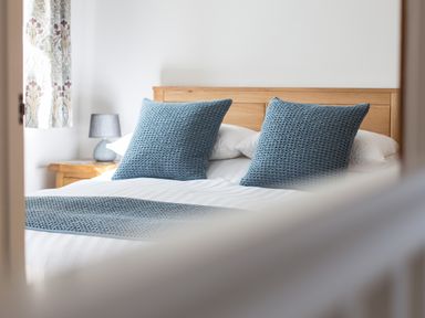 A bedroom with a wooden bed frame blue pillows and a bedside table with a lamp at Cornish Views in Camborne