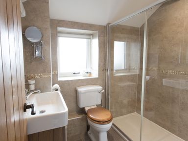 A bathroom with a toilet with wooden seat a sink a shower enclosure and a window at Cornish Views in Camborne