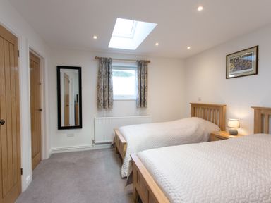 A bedroom with two single beds a lamp on a bedside table a window with curtains and a wall mirror at Cornish Views in Camborne