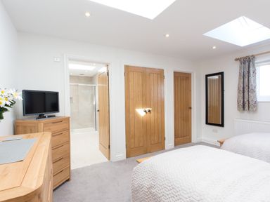 A bedroom with two beds a dresser with a television and doors leading to a bathroom and closets at Cornish Views in Camborne