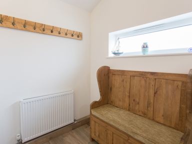 A small room with a wooden bench with a cushion a wall-mounted coat rack and a window sill with decorative items at Cornish Views in Camborne