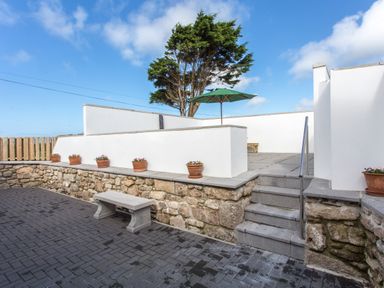 An outdoor patio area with stone bench stone steps and terracotta flower pots with a green umbrella and tall tree at Cornish Views in Camborne