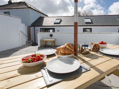 An outdoor picnic table set with plates cutlery croissants strawberries and a teapot at Cornish Views in Camborne