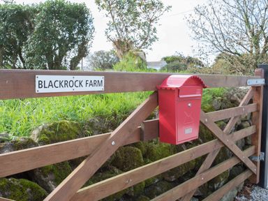 A wooden farm gate with a red mailbox and a sign that reads Blackrock Farm at Cornish Views in Camborne