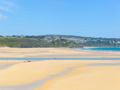 A sandy beach with small pools of water and a distant view of houses on green hills at Cornish Views in Camborne