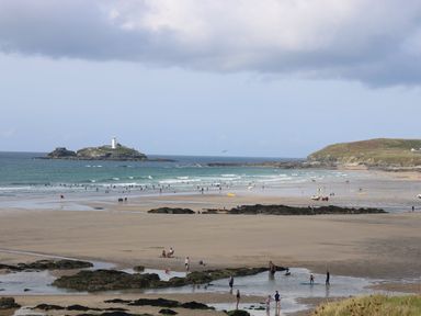 A beach with people on the sand and in the water with a small island and lighthouse in the background at Cornish Views in Camborne