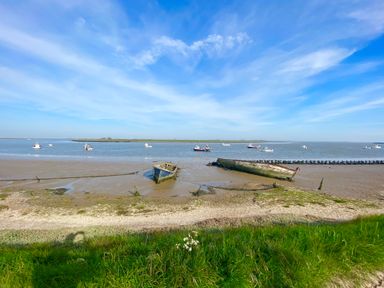 A shoreline with two abandoned boats on the sand and several boats on the water at Mundays in Orford