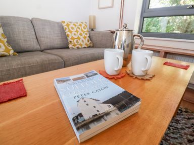 A wooden coffee table with a book named Suffolk Coast Walk two white mugs and a silver pot in a living room with a gray sofa and yellow cushions at Mundays in Orford