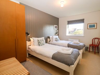 A bedroom with two single beds a wooden wardrobe a red chair and a window at Mundays in Orford