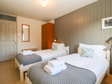 A bedroom with two single beds gray striped blankets white towels wooden wardrobe and wall mirror at Mundays Orford