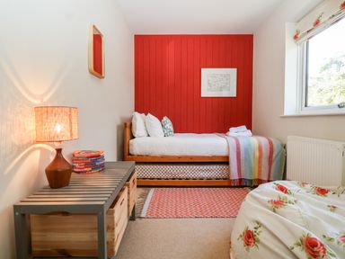 A bedroom with a single bed and colorful striped blanket a wooden bench with a lamp and a basket a window and floral bean bag at Mundays in Orford