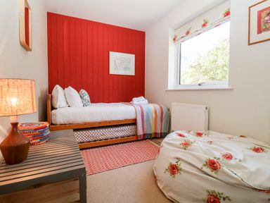 A small bedroom with a single bed against a red wall a nightstand with a lamp a window and a floral beanbag chair at Mundays in Orford