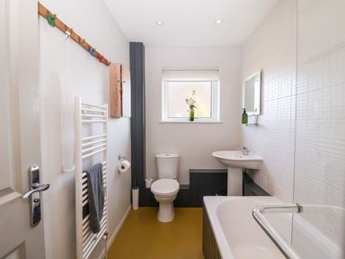 A bathroom with a toilet sink and bathtub with a window above the toilet and a towel rack on the wall at Mundays in Orford