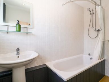 A bathroom with a white sink pedestal a green soap dispenser a bathtub with a shower and a white shower curtain at Mundays in Orford