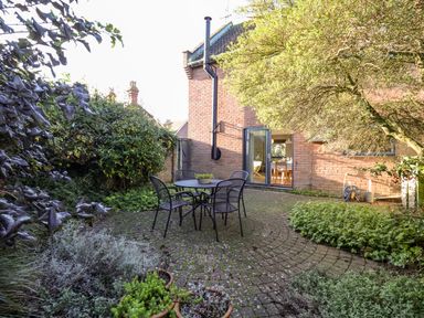 An outdoor patio with a round table and four chairs surrounded by plants and trees at Mundays in Orford