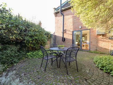 A patio area with a round table and four chairs outside a brick house at Mundays Orford