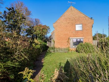 A brick house with two windows a grassy lawn and bushes under a clear blue sky at Mundays in Orford