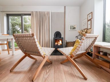 A living room with two woven wooden chairs facing a wood stove with a fire at Mundays in Orford