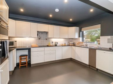A kitchen with white cabinets gray countertops and a window overlooking a garden at Mundays in Orford
