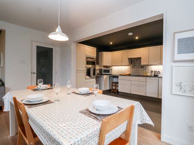A dining table set with plates bowls and glasses near a kitchen with white cabinets and appliances at Mundays in Orford