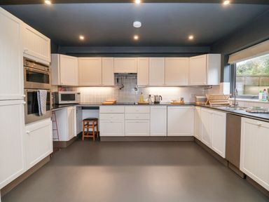 A kitchen with white cabinets, built-in ovens, microwave, stool, countertop appliances, and a window at Mundays in Orford