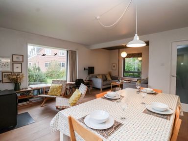 A dining area with a table set for four and a living room with chairs and sofas near large windows at Mundays in Orford