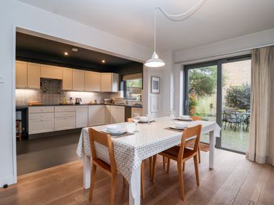 A dining area with a set table and wooden chairs next to a kitchen with white cabinets and a sliding glass door showing a patio at Mundays in Orford