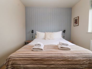 A bed with white pillows and folded towels with a striped blanket against a blue paneled wall at Mundays in Orford