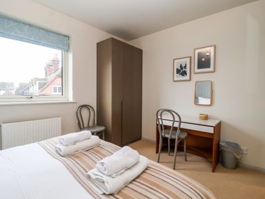 A bedroom with a bed with folded towels a wardrobe a desk a chair a trash can and two framed pictures on the wall at Mundays in Orford