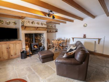 A living room with a stone fireplace and wood stove a brown leather sofa a wooden dining table with chairs and a television on a wooden cabinet at Swinhope View in Hexham