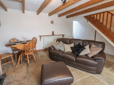 A living room with a brown leather sofa and ottoman a wooden dining table with chairs and exposed wooden ceiling beams at Swinhope View in Hexham