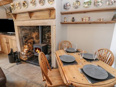 A dining area with a wooden table and chairs set with plates and glasses next to a wood burning stove and shelves with decorative items at Swinhope View in Hexham