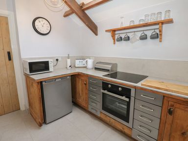 A kitchen corner with a microwave on the counter a mini fridge an oven a stovetop and shelves with mugs and glasses at Swinhope View in Hexham