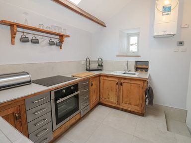 A kitchen with wooden cabinets an electric oven a sink and a shelf with mugs and glasses at Swinhope View in Hexham