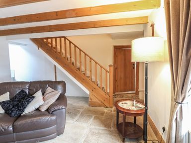 A living room with a brown leather sofa cushions wooden stairs a small round table and a floor lamp at Swinhope View in Hexham