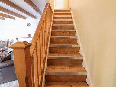 A wooden staircase with metal strips on the edge next to a wooden railing with a living area visible in the background at Swinhope View in Hexham