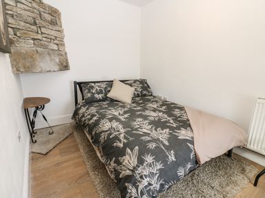A bedroom with a double bed covered with a dark floral duvet and light pillow next to a stone feature and wooden floor at Swinhope View in Hexham