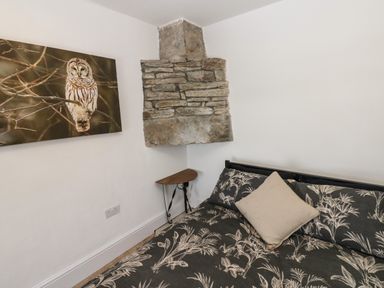 A corner of a room with a bed with patterned bedding a small triangular wooden table a stone chimney breast and an owl picture on the wall at Swinhope View in Hexham