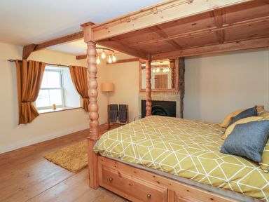 A bedroom with a wooden four-poster bed yellow patterned bedding a window with curtains a fireplace and a floor lamp at Swinhope View in Hexham