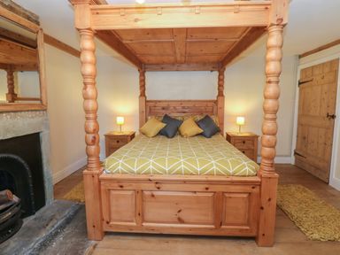 A bedroom with a four poster wooden bed with yellow and gray pillows and matching patterned bedspread at Swinhope View in Hexham
