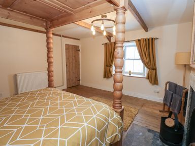 A bedroom with a wooden four poster bed a window with curtains a wooden door and wooden floor at Swinhope View in Hexham