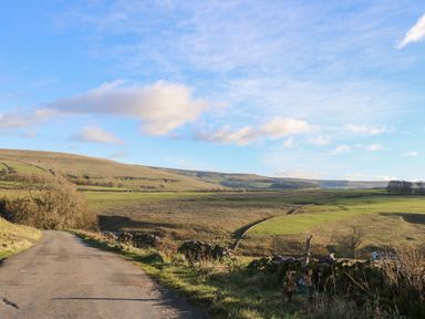 A country road leading through fields and hills under a blue sky at Swinhope View in Hexham