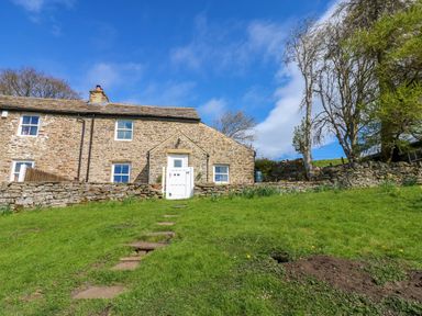 A stone house with a white gate and stone steps leading up to it surrounded by grass and trees at Swinhope View in Hexham