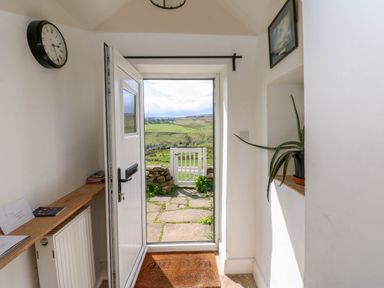 A hallway with an open door showing a stone path and green fields outside at Swinhope View in Hexham