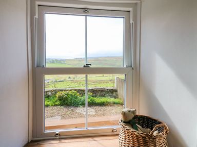 A window with a view of a garden and fields outside and a teddy bear in a wicker basket nearby at Swinhope View in Hexham